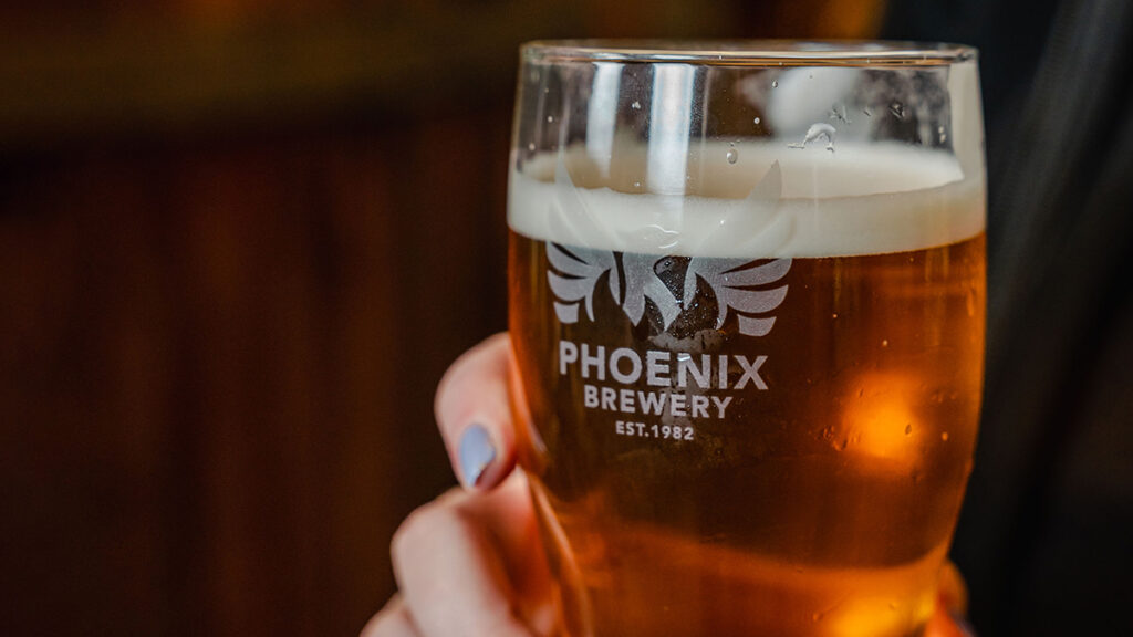 Close up of female holding a custom branded Phoenix Brewery pint glass filled with Phoenix Brewery IPA