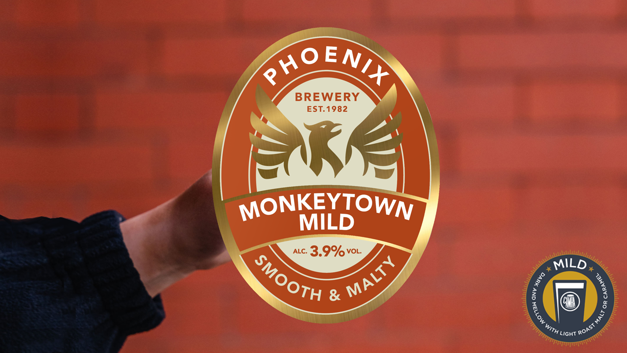 A hand holding the Phoenix Brewery Monkeytown Mild pump clip against a red bricked wall