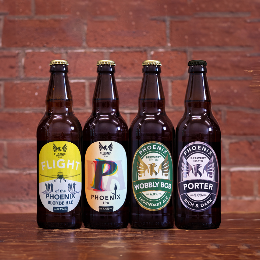 Four bottles of Phoenix Brewery beers lined up against a brick wall, featuring Flight Blonde Ale, Phoenix IPA, Wobbly Bob, and Porter