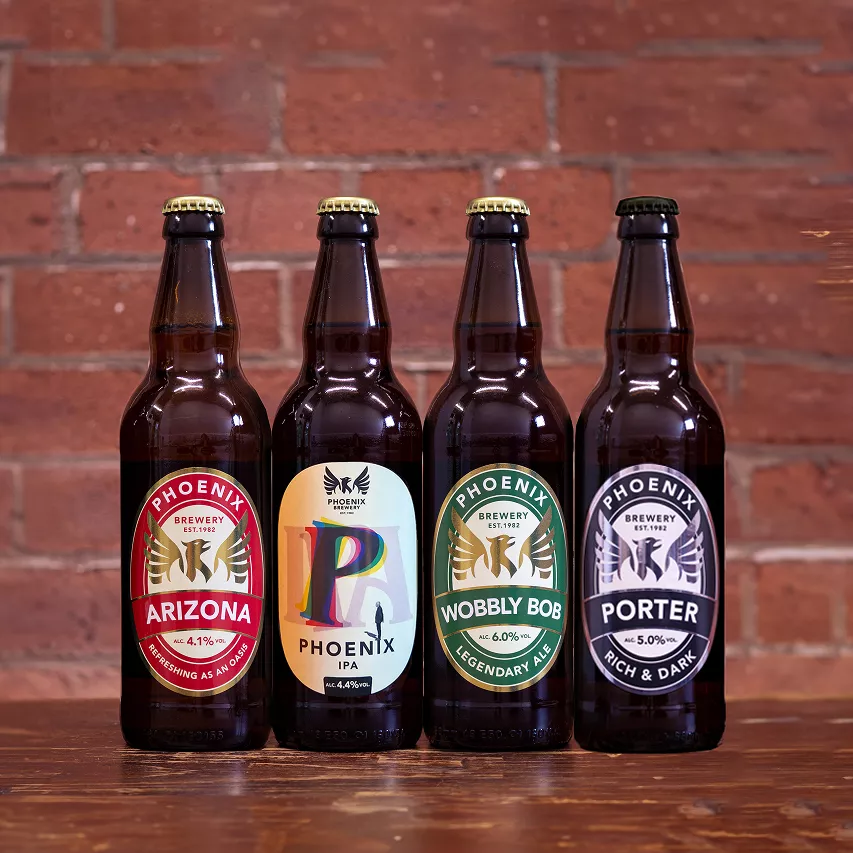 Four bottles of Phoenix Brewery beers lined up against a brick wall, featuring Arizona, Phoenix IPA, Wobbly Bob, and Porter.