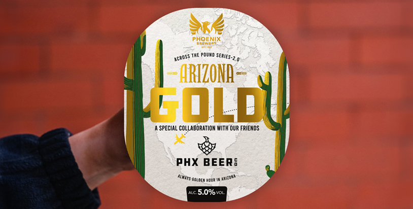 A hand holding the Phoenix Brewery Arizona Gold pump clip against a red bricked wall