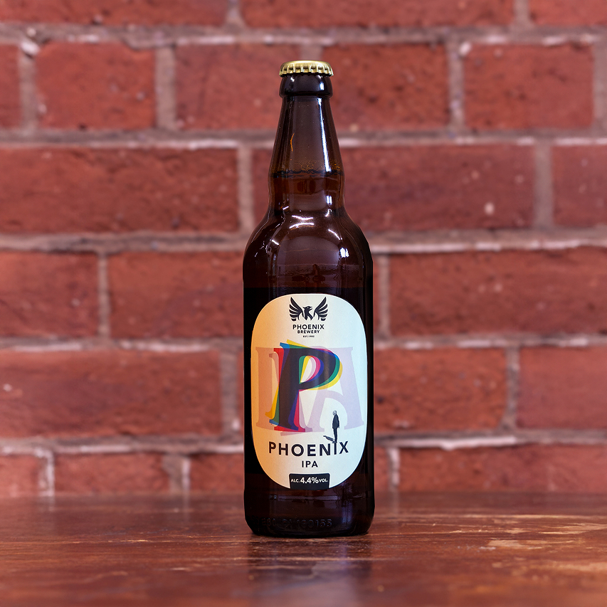 A bottle of Phoenix IPA from Phoenix Brewery placed on a wooden table with a brick wall in the background.