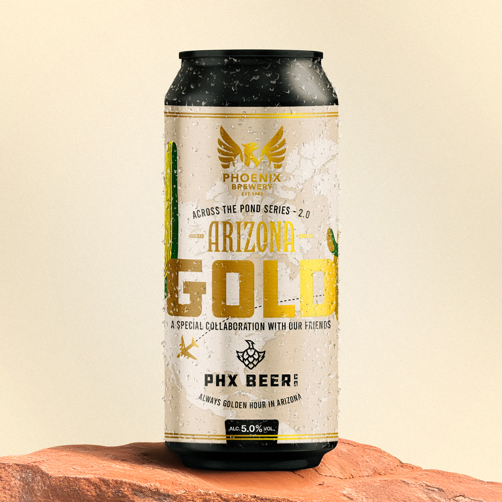 A close-up of a condensation-covered can of Phoenix Brewery’s “Arizona Gold” beer, placed on a red sandstone surface. The label features gold typography, a cactus illustration, and a collaboration note with PHX Beer Co., set against a clean, light cream background.