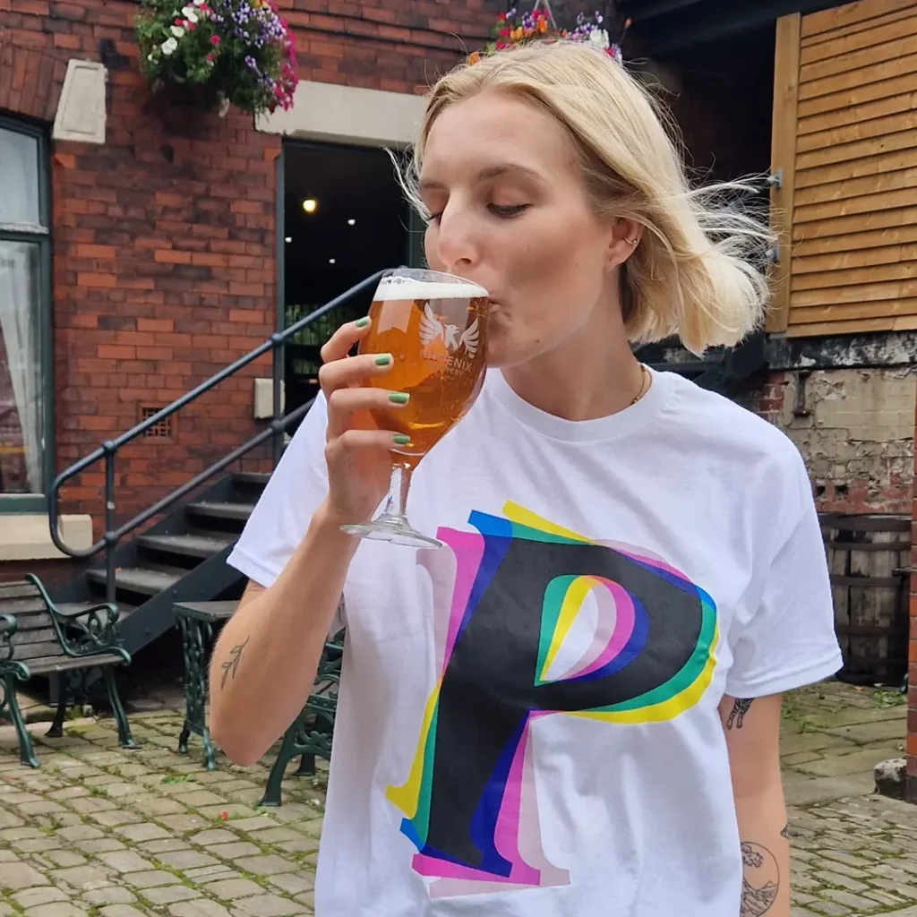 Woman drinking from a Phoenix Brewery branded pint glass outdoors, wearing the white P-logo t-shirt